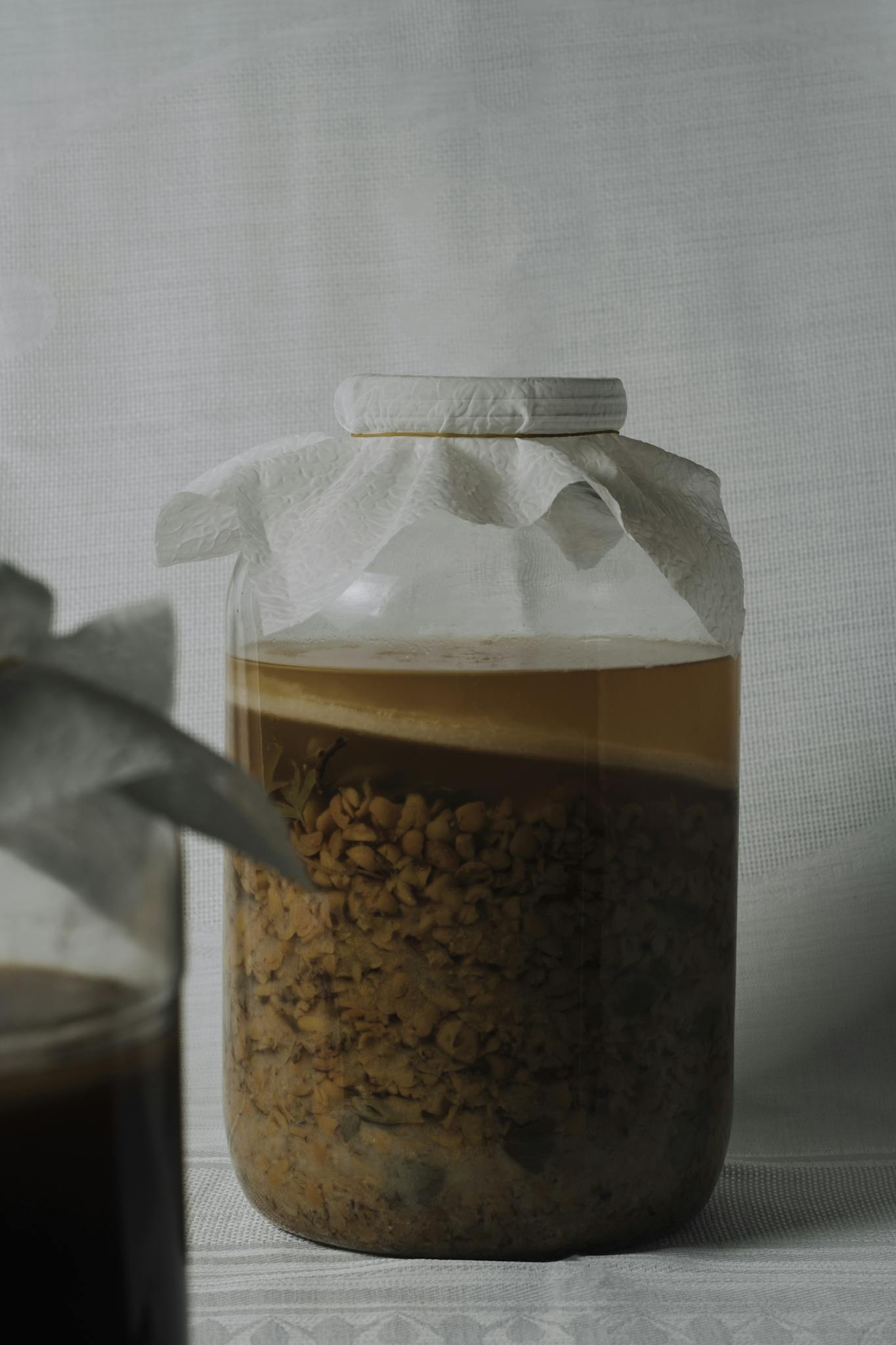 Glass jar with fermenting mixture on plain background, showcasing fermentation process.