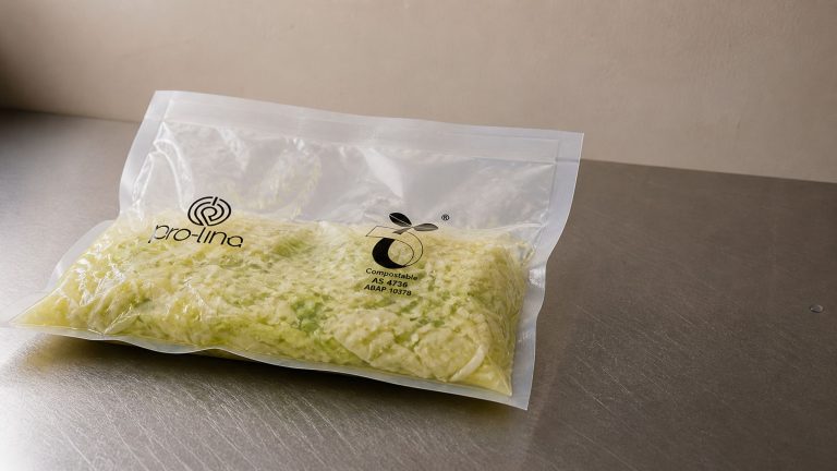 Pro-Line compostable vacuum bag of shredded green cabbage on a brushed stainless steel bench, post-vacuum sealed, AS 4736 compostable certification mark visible.